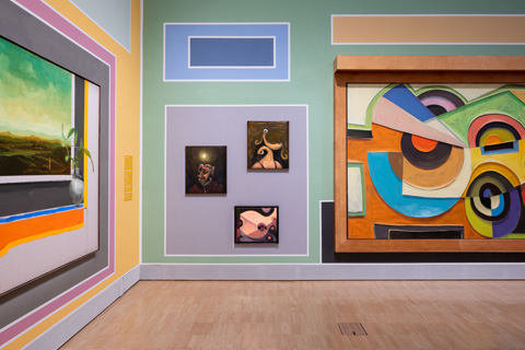 Eine bunte Wand in der Ausstellungshalle mit mehreren kleinen und großen Gemälden.