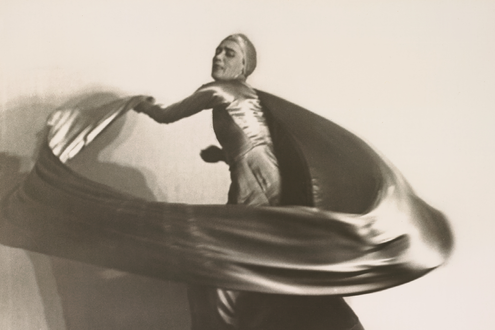 Fotografie einer tanzenden Frau in weiter, fließender Kleidung in ausdrucksstarker Pose.