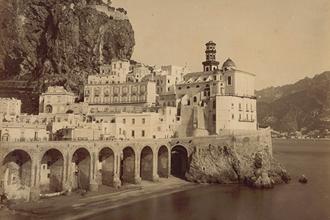 Fotografie einer italienischen Stadt am Wasser, die in den Fels gebaut ist.