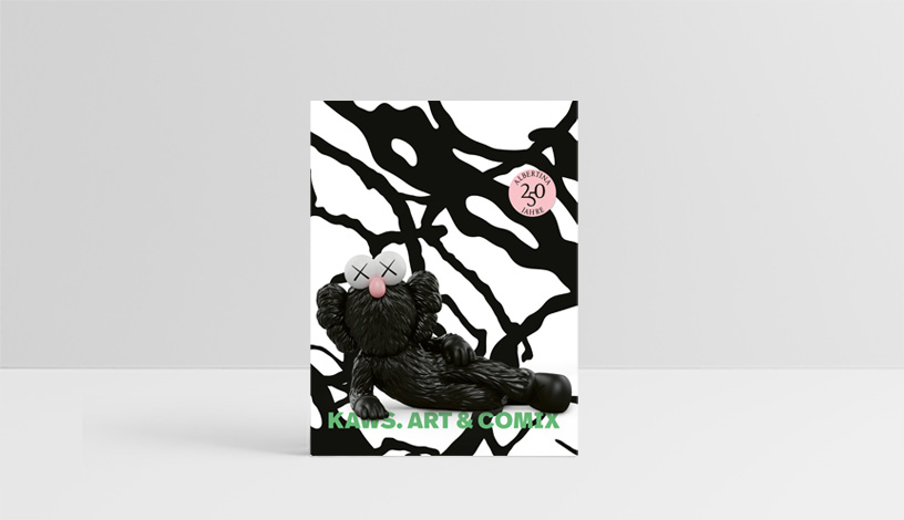 Der Ausstellungskatalog vor einem grauen Hintergrund. Am Katalog ist eine liegende KAWS-Skulptur zu sehen, ein runder, rosa Sticker mit dem 250 Jahre ALBERTINA Logo und neon-grünem Schriftzug 