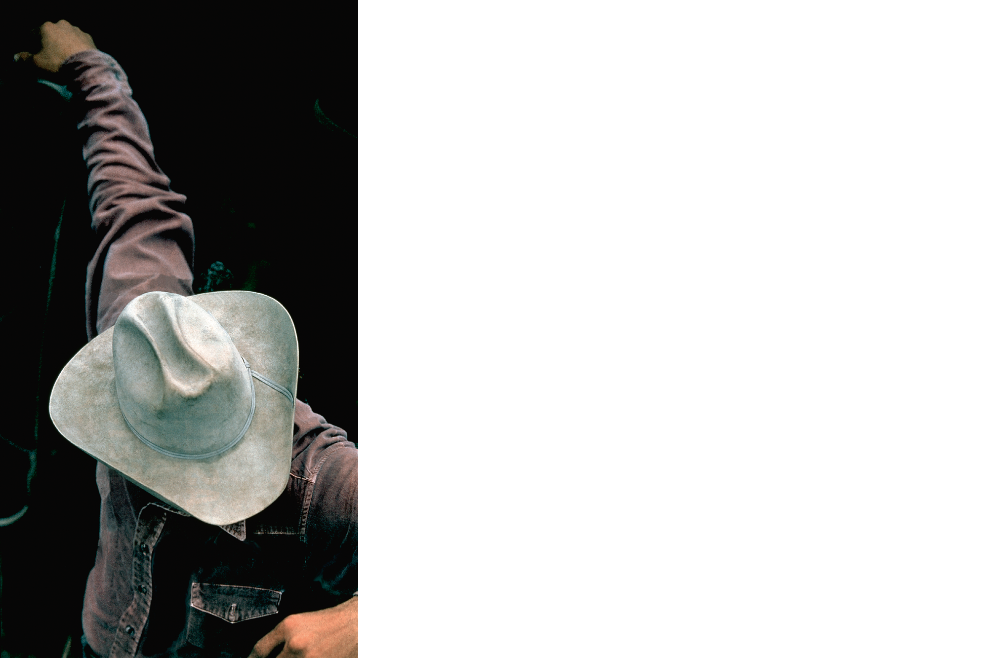 Fotografie eines Cowboys im Jeanshemd und Hut, nach unten blickend, ein Arm nach oben gestreckt.