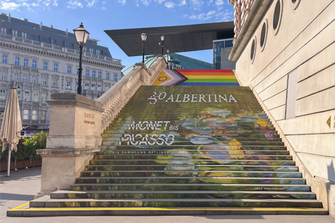 Foto der ALBERTINA Treppe mit dem Seerosenteich von Monet und der Auschrift 250 ALBERTINA Monet bis Picasso und darüber, am oberen Ende der Treppe die Pride-Flagge.