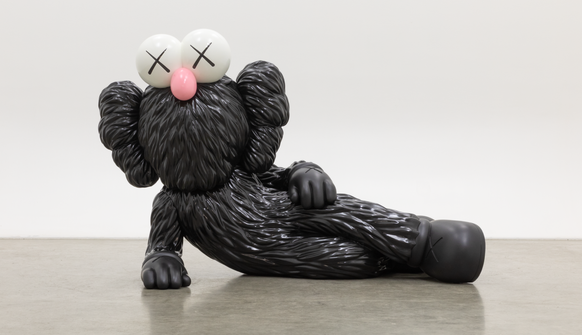 Skulptur einer seitlich aufgestützt, liegenden, schwarz pelzigen Comicfigur mit einer pinken Stupsnase und X-Augen.
